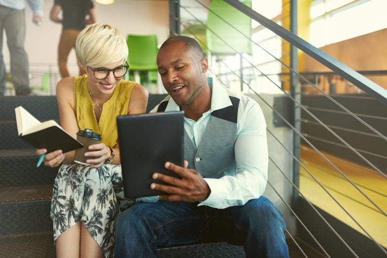 Two creative millenial small business owners working on social media strategy using a digital tablet while sitting in staircase.jpeg